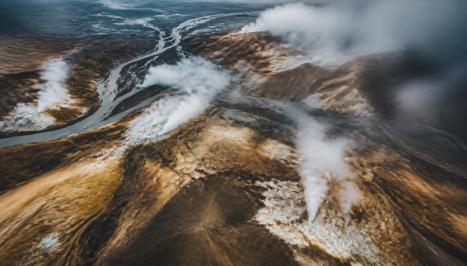 Aerial view of a vast Icelandic geothermal field with steaming vents, mineral-stained ground and braided glacial rivers